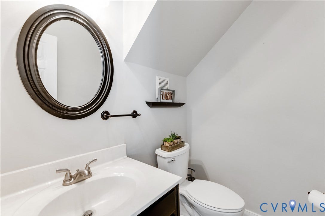 11611 Riverpark Way, Chesterfield, VA 23838 Powder room featuring a white single-basin vanity with a brushed nickel faucet, an oval mirror with a dark wood frame, and a dark wood floating shelf