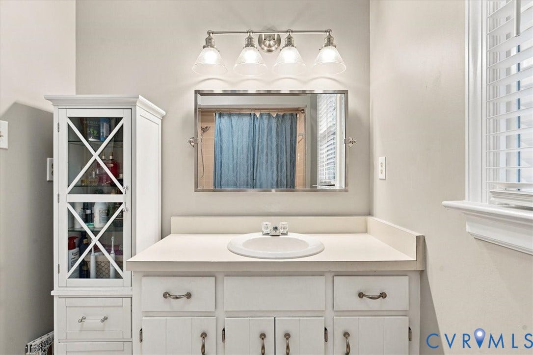 10204 Steuben Drive, Henrico, VA 23060 Bathroom vanity featuring a white countertop with an integrated sink, white cabinetry with various hardware, and a framed mirror