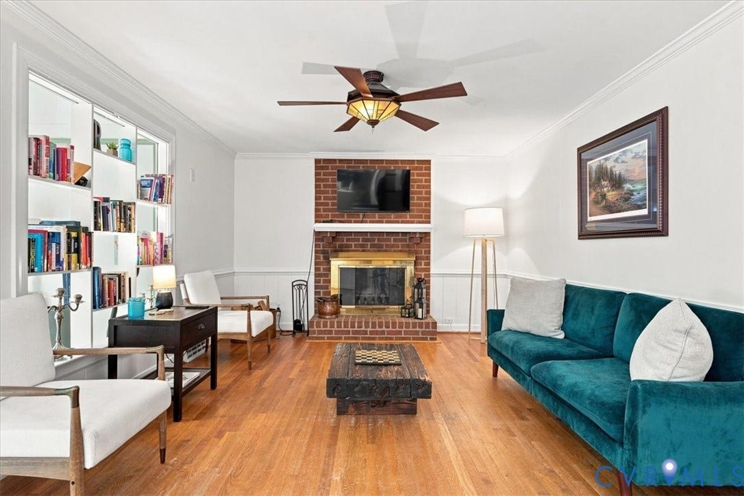 10204 Steuben Drive, Henrico, VA 23060 Bright living area featuring wood-finish flooring, a brick fireplace with a brass firebox, built-in shelving, crown molding, and a ceiling fan with integrated lighting