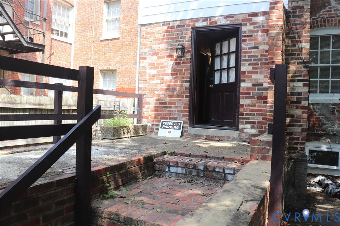 1119 W Grace Street, The Fan District, Richmond, VA 23220 Brick exterior with a dark-paneled entry door, a prominent outdoor light fixture, and a concrete patio area