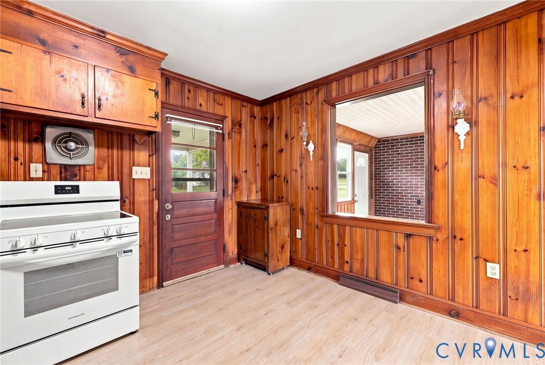 5002 Glendale Avenue, Dinwiddie, VA 23803 Wood paneling throughout, built-in wooden cabinetry, white freestanding range, light wood-finish flooring, and a pass-through window