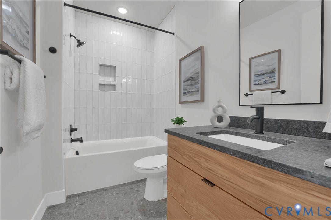 4506 1/2 Grove Avenue, Munford On Grove, Richmond, VA 23221 Full bathroom featuring a rectangular sink set in a dark stone countertop, a wood-finish vanity with drawer storage, a framed mirror, and a shower-tub combination with white vertical subway tile