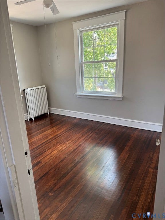 3118 Barton Avenue, Brookland Park, Richmond, VA 23222 Bedroom #5 2nd floor, bright, light-filled bedroom featuring hardwood flooring with warm wood-grain finish, large double-hung window with white trim framing natural greenery, fresh neutral wall paint, ceiling fan, and baseboard heating element