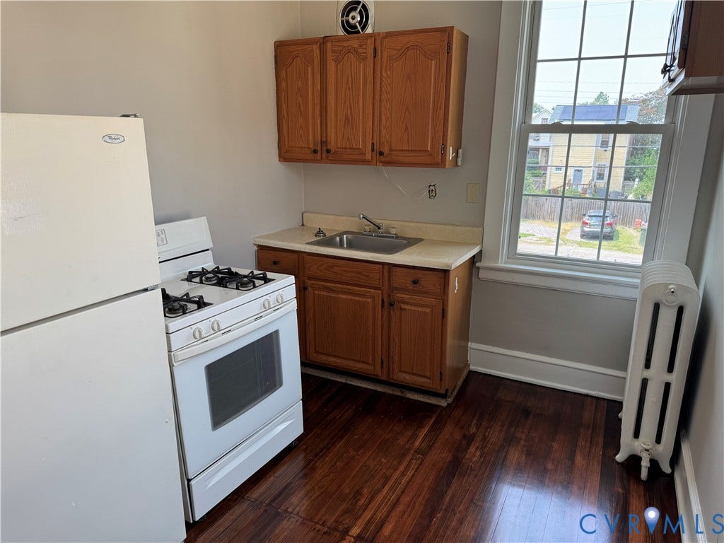 3118 Barton Avenue, Brookland Park, Richmond, VA 23222 Compact kitchen featuring white gas range with oven, white refrigerator, wood cabinetry with upper and lower storage, laminate countertop with integrated sink, wood-finish flooring, and large window with natural light and neighborhood views