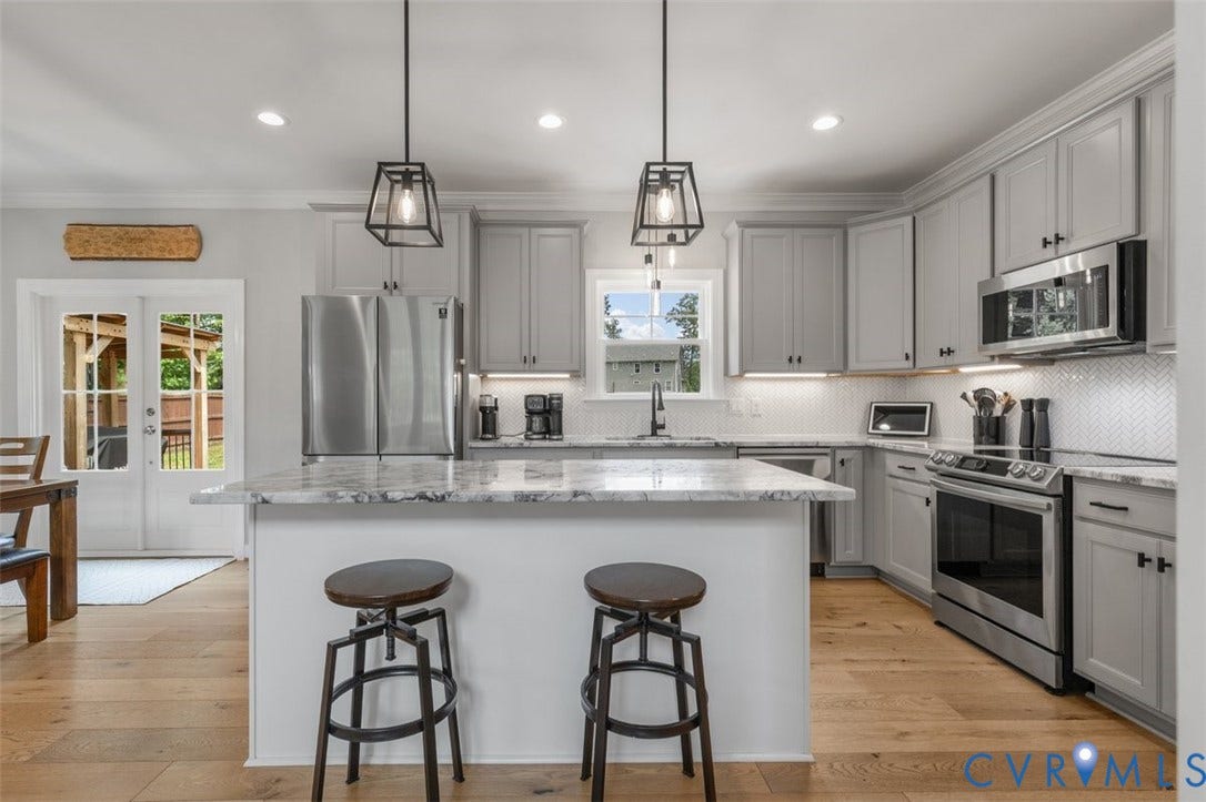 9081 Deerlake Drive, Charming, New Kent, VA 23124 Kitchen featuring a central island with countertop seating, light wood-finish flooring, light gray cabinetry, stainless steel appliances, and a herringbone pattern tile backsplash