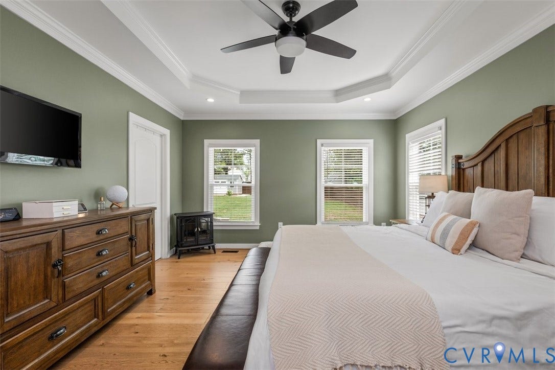 9081 Deerlake Drive, Charming, New Kent, VA 23124 Spacious room featuring a tray ceiling with recessed lighting and a ceiling fan, two windows with blinds, wood-finish flooring, and a dark wood headboard