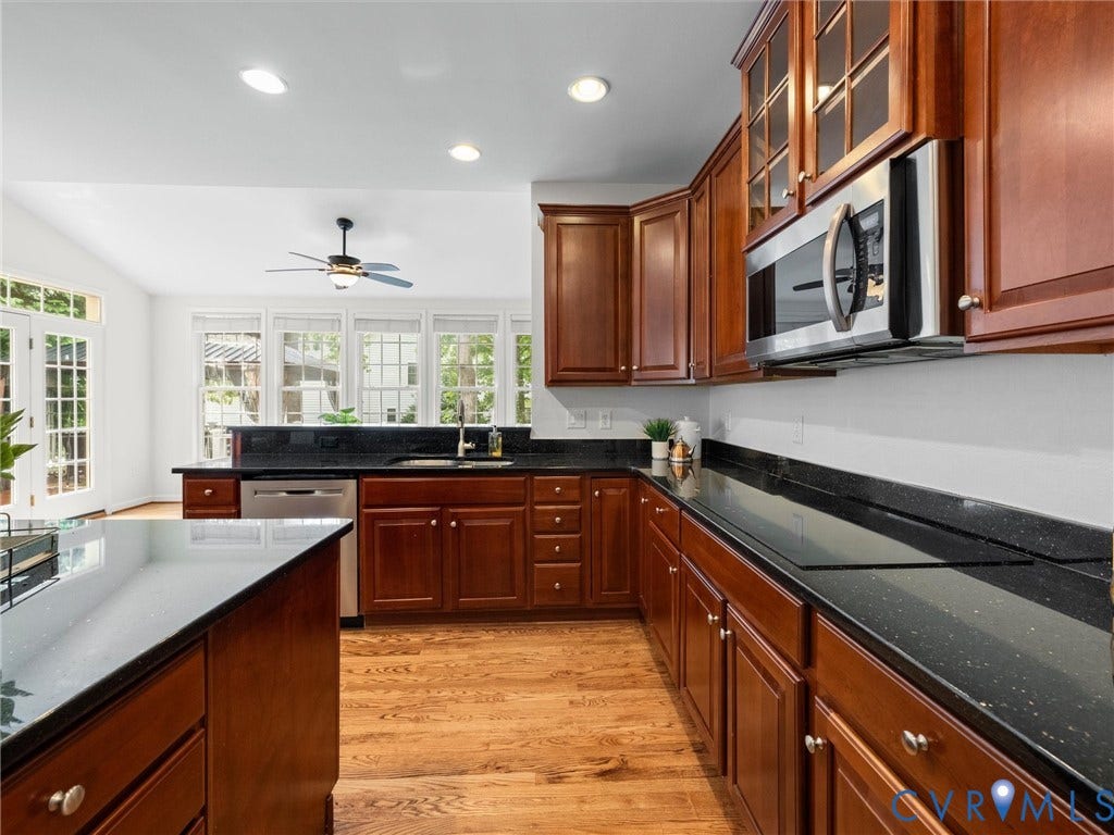 6100 Lilting Branch Way, Moseley, VA 23120 Kitchen featuring dark wood cabinetry, a built-in stainless steel microwave, black countertops, and wood-finish flooring