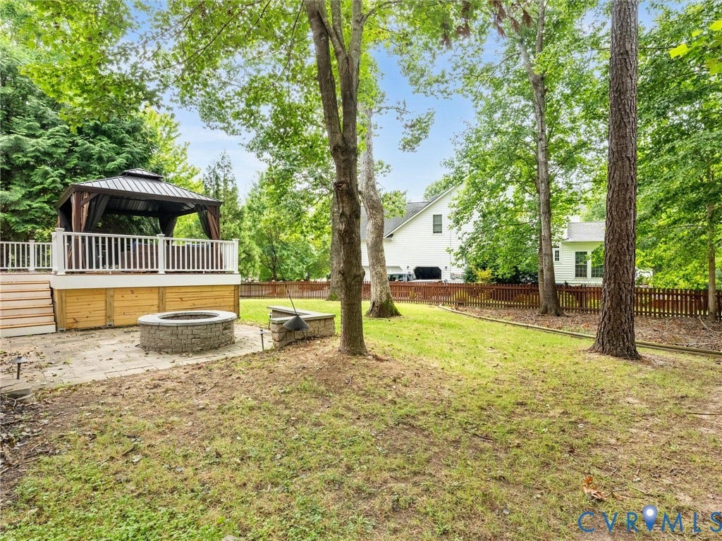 6100 Lilting Branch Way, Moseley, VA 23120 Expansive backyard featuring a built-in stone fire pit, wood deck with white railing, and a permanent gazebo structure