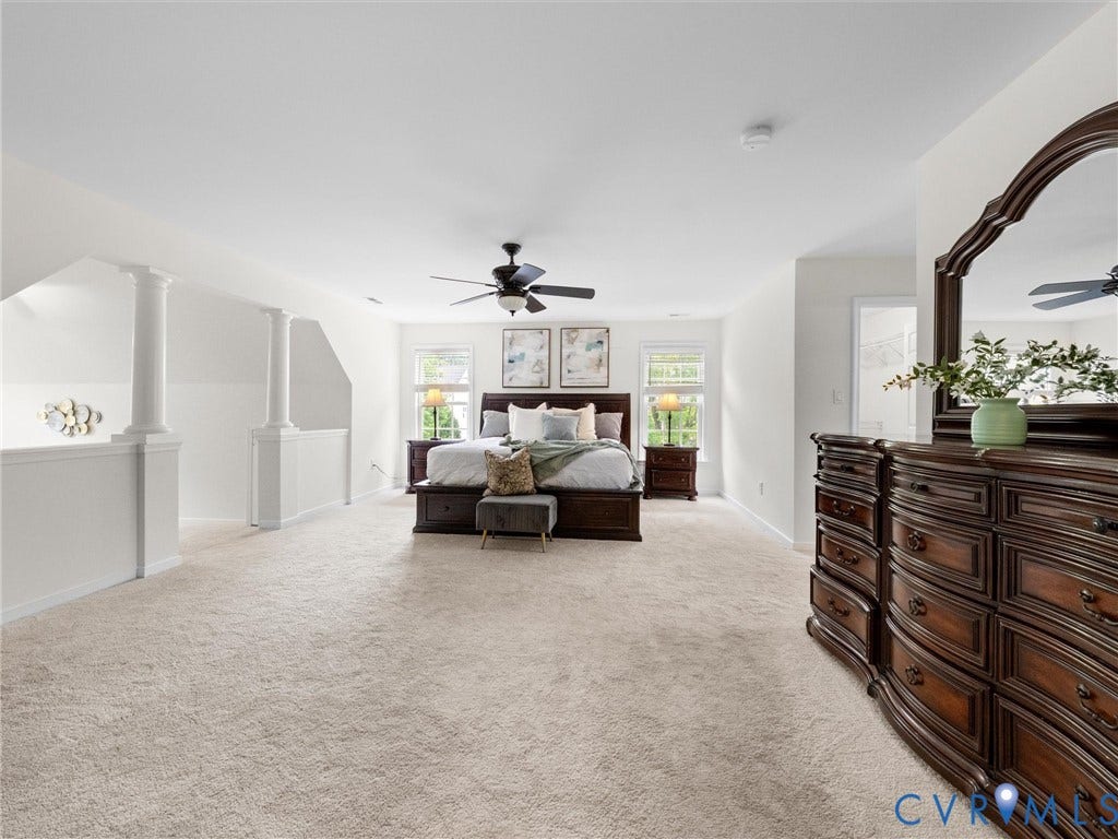 6100 Lilting Branch Way, Moseley, VA 23120 Spacious carpeted room featuring a ceiling fan, multiple windows, and a partial balustrade with decorative columns