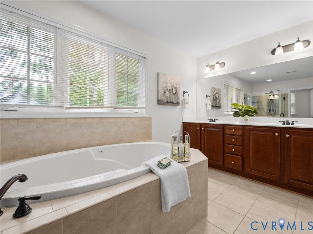 6100 Lilting Branch Way, Moseley, VA 23120 Built-in soaking tub with surrounding tile, dual vanity with wood cabinetry, and a large wall-mounted mirror