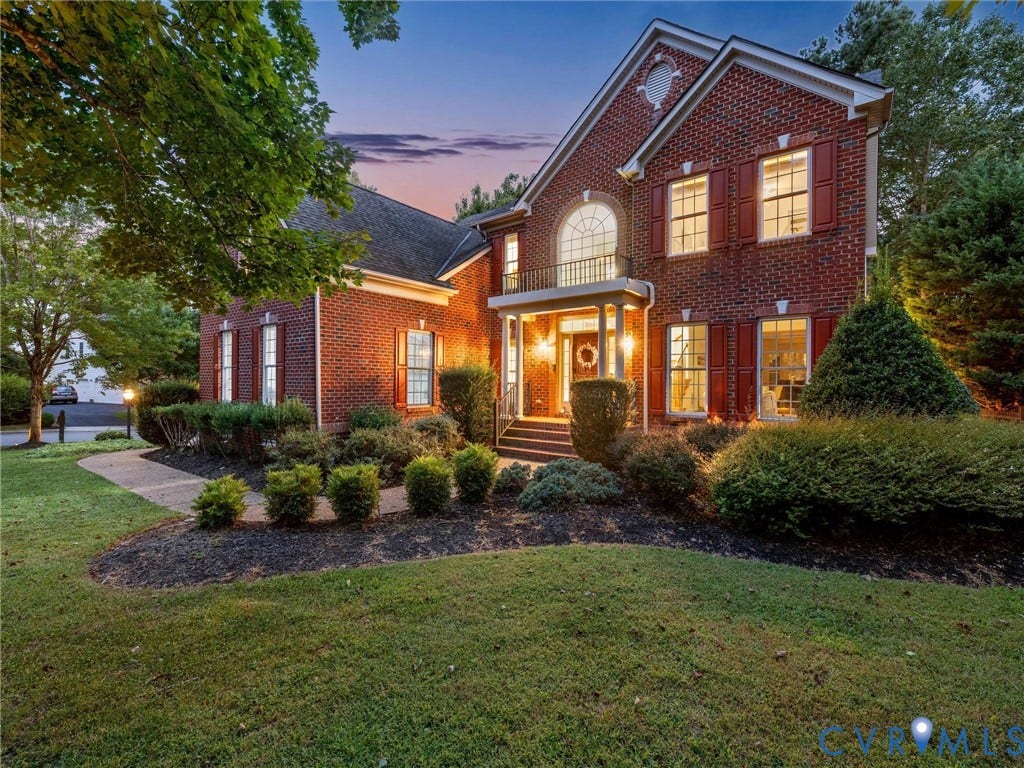 6100 Lilting Branch Way, Moseley, VA 23120 Brick exterior featuring red shutters, a decorative arched window, a covered portico, and a second-story balcony