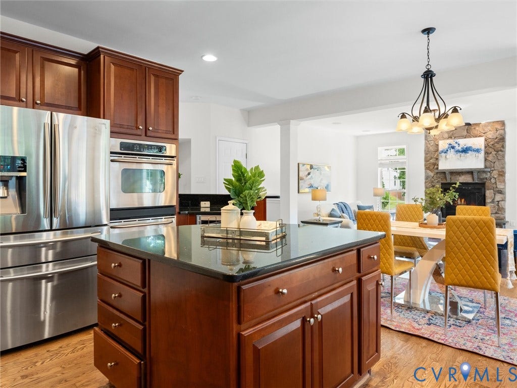 6100 Lilting Branch Way, Moseley, VA 23120 Hardwood-finish flooring, cherry wood cabinetry, stainless steel appliances, a kitchen island with a dark countertop, and a stone fireplace