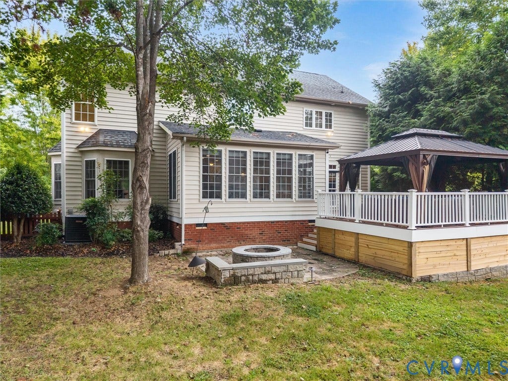 6100 Lilting Branch Way, Moseley, VA 23120 Rear exterior with siding, a sunroom with multiple windows, an elevated deck featuring white railings, a built-in gazebo, and a stone-lined fire pit on a paver patio