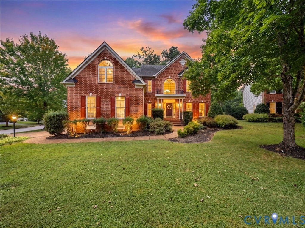 6100 Lilting Branch Way, Moseley, VA 23120 Brick facade residence featuring a covered entry, arched window elements, mature landscaping, and an expansive lawn
