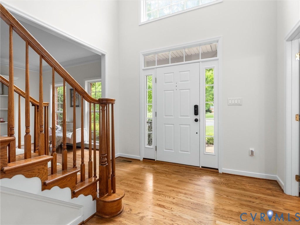 6100 Lilting Branch Way, Moseley, VA 23120 Two-story foyer featuring hardwood flooring, a white paneled front door with sidelights and transom windows, and a hardwood staircase with a decorative newel post