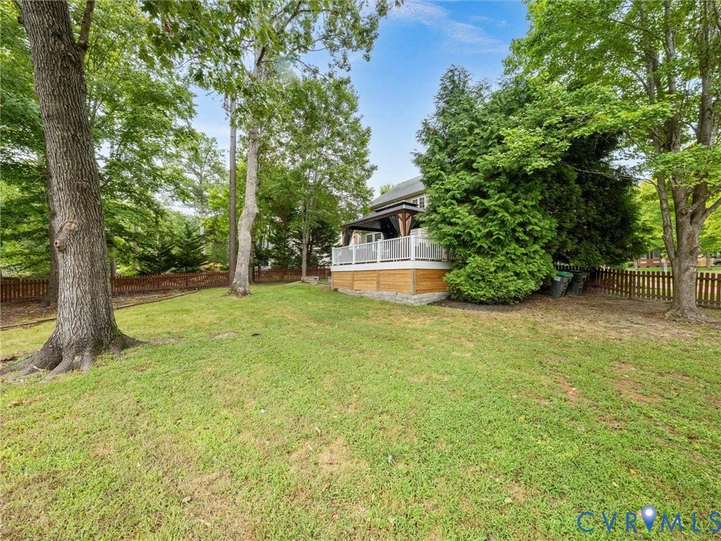 6100 Lilting Branch Way, Moseley, VA 23120 Expansive grassy yard with mature trees, a wood-slat privacy fence, and a raised exterior deck featuring white railings