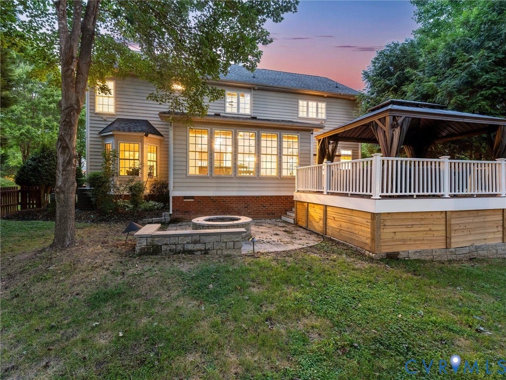 6100 Lilting Branch Way, Moseley, VA 23120 Rear exterior with siding, a bay window, a sunroom with multiple windows, a raised deck with white railings, and a built-in fire pit with a paver surround