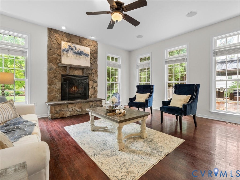 6100 Lilting Branch Way, Moseley, VA 23120 Stone-clad fireplace with a hearth, dark wood-finish flooring, multiple pane windows, ceiling fan with integrated lighting, and recessed ceiling lights