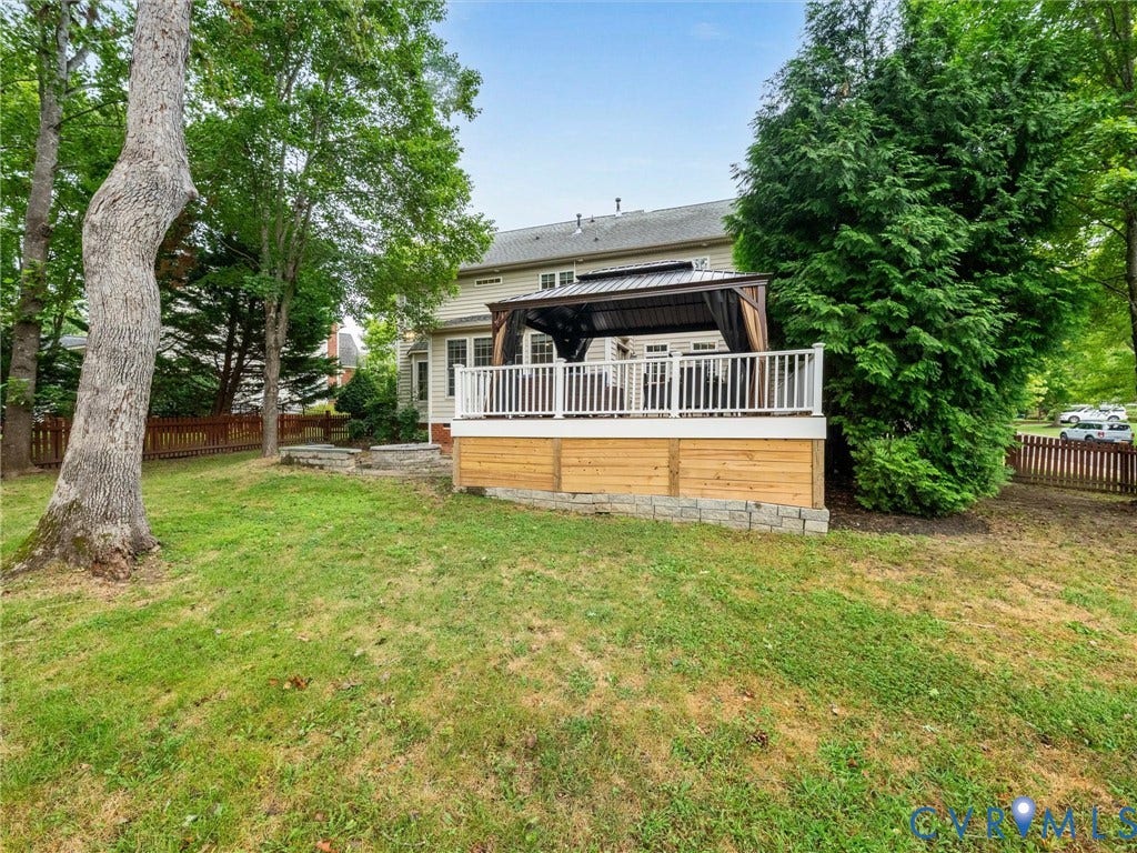 6100 Lilting Branch Way, Moseley, VA 23120 Expansive lawn with mature trees, wooden privacy fence, multi-level composite deck, white railing, and a built-in gazebo with a metal roof