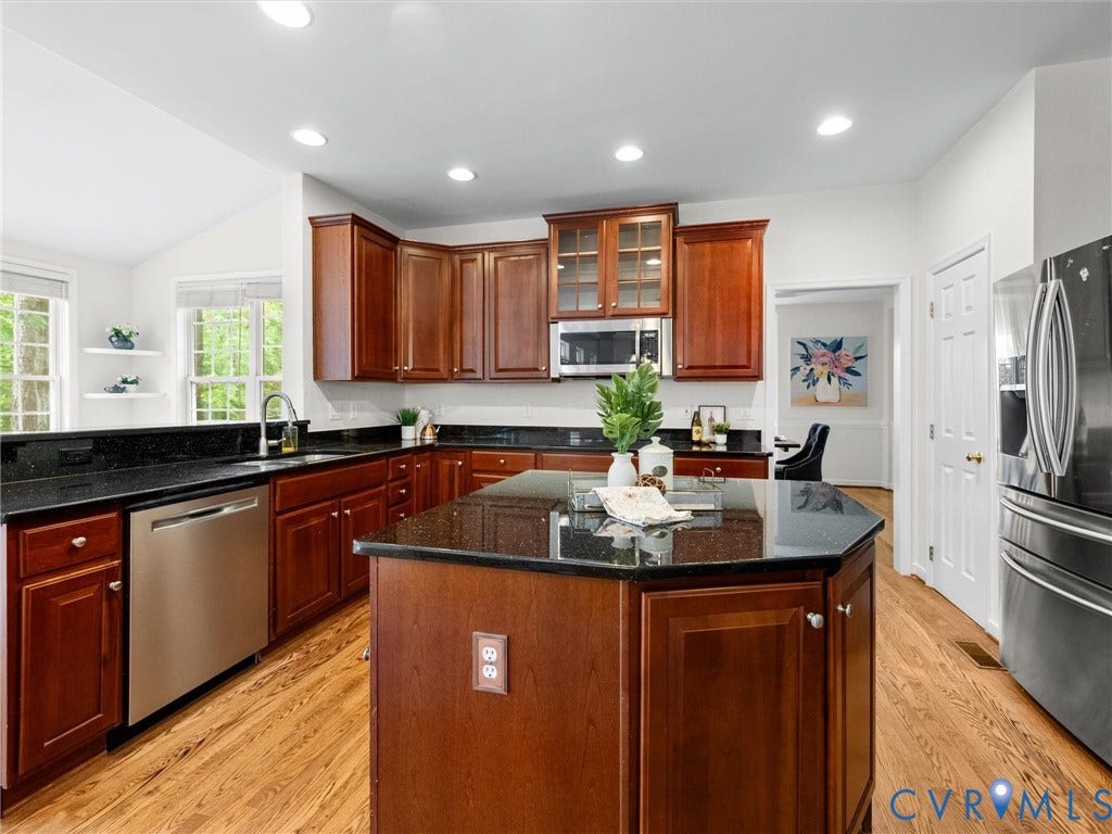 6100 Lilting Branch Way, Moseley, VA 23120 Kitchen featuring an angled island, rich wood cabinetry, dark countertops, stainless steel appliances, and wood-finish flooring