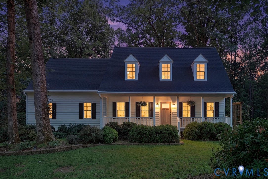 1915 Norwood Creek Drive, Powhatan, VA 23139 Front exterior featuring white siding, a covered porch with white railings, a dark roof, three dormer windows, and a landscaped front yard with mature trees