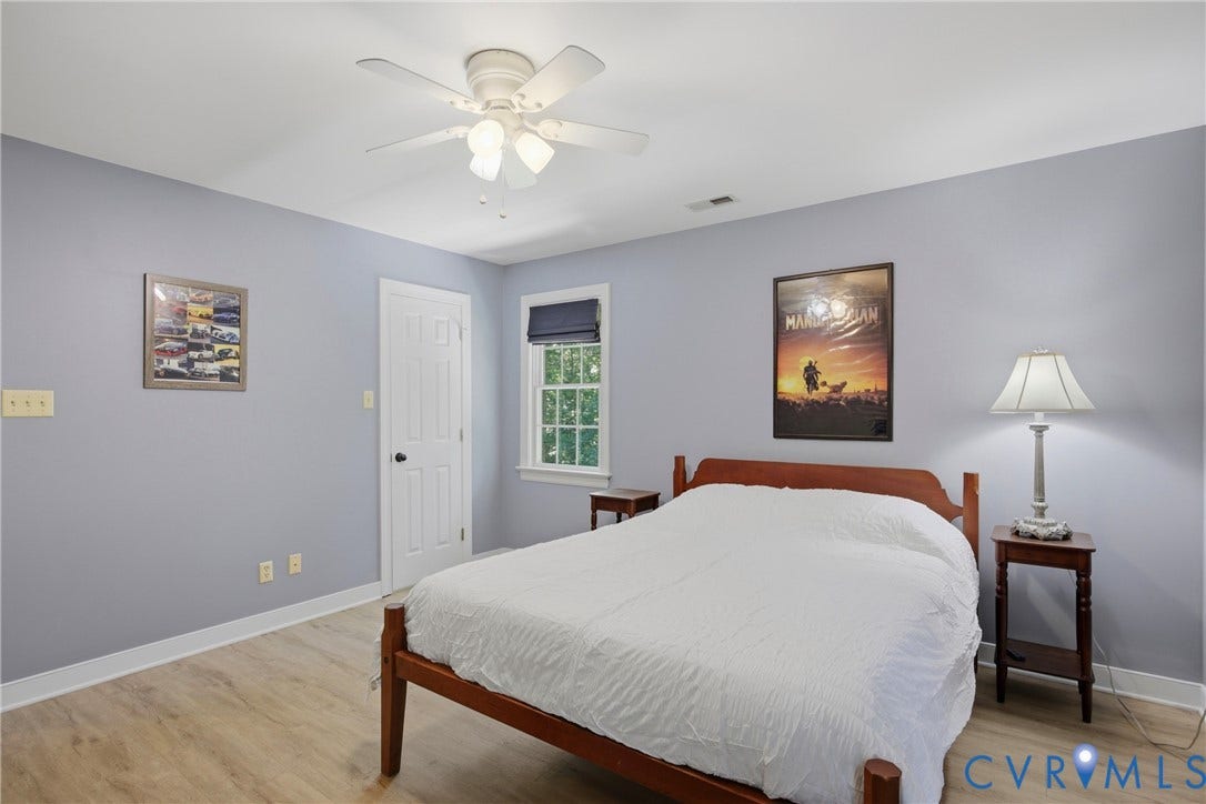 1915 Norwood Creek Drive, Powhatan, VA 23139 Bedroom featuring light-tone wood-finish flooring, a ceiling fan with integrated lighting, a single window with a dark roller shade, and a white paneled door