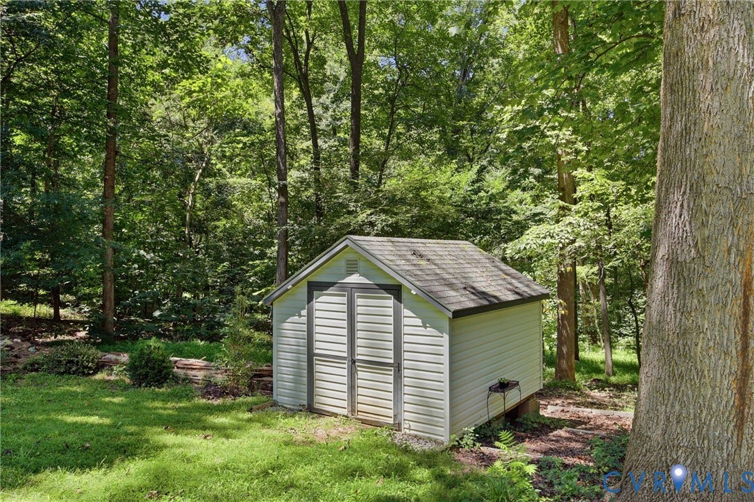 1915 Norwood Creek Drive, Powhatan, VA 23139 Detached storage shed with siding exterior, double doors, and shingle roof, complemented by a wooded backdrop and mature trees