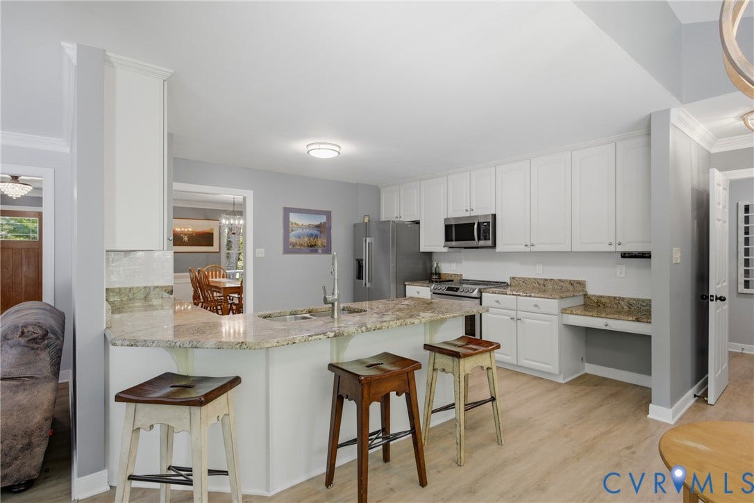 1915 Norwood Creek Drive, Powhatan, VA 23139 Kitchen featuring a breakfast bar with stone countertops, white shaker cabinetry, stainless steel appliances, and light wood-finish flooring