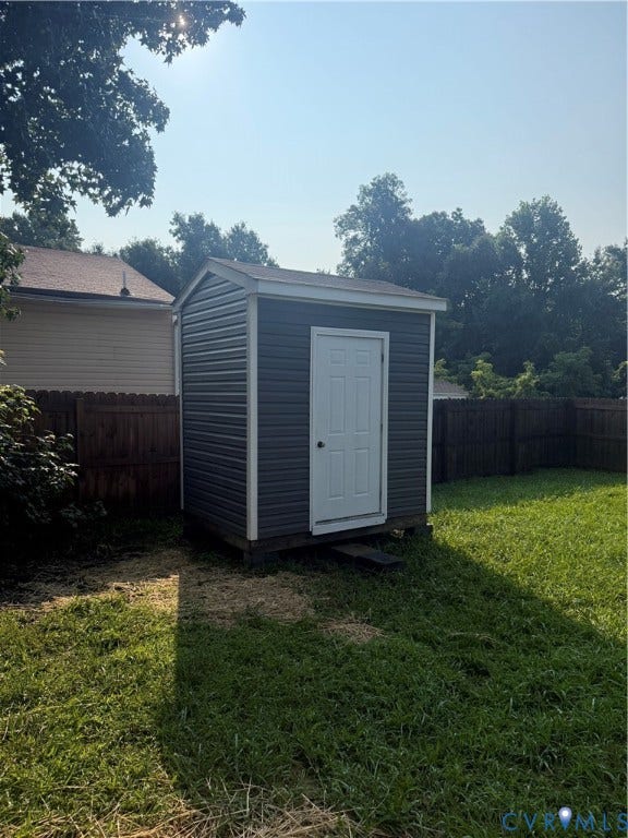 Backyard storage shed featuring dark gray siding, a white entry door, and a light-colored roof