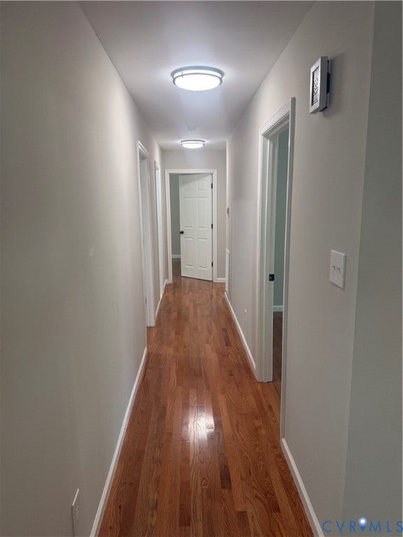 Hallway featuring wood-finish flooring, light gray walls, white trim, and ceiling-mounted flush lighting
