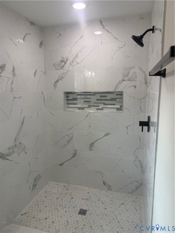 Walk-in shower featuring large format veined wall tiles, a recessed niche with mosaic tile inlay, pebble-style floor tiling, matte black shower fixtures, and integrated ceiling lighting