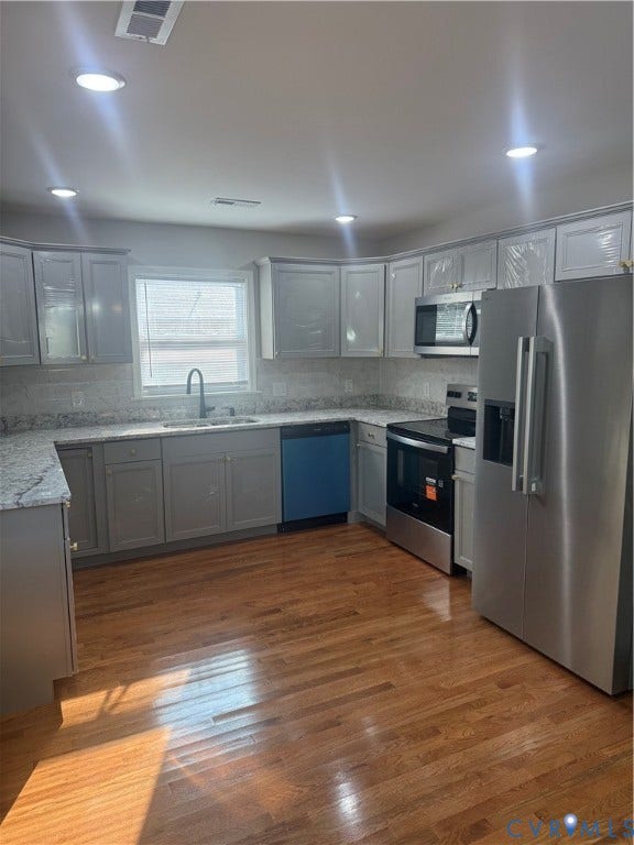 Kitchen featuring recessed lighting, a stainless steel appliance suite, light gray cabinetry, light-toned countertops, and wood-finish flooring