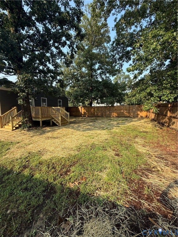 Expansive outdoor space featuring a large wooden deck with dual staircases, a full privacy fence, and mature trees providing natural shade