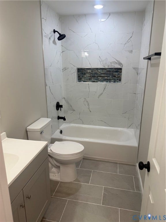 Full bathroom featuring a white porcelain tub, an integrated tiled shower niche with mosaic accents, and a single vanity with a white countertop