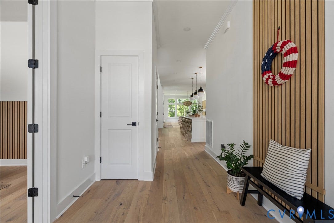 18312 Barrin Court, Barrington, Moseley, VA 23120 Bright, open hallway featuring warm wood-finish flooring, white interior doors with matte black hardware, and vertical wood slat wall paneling