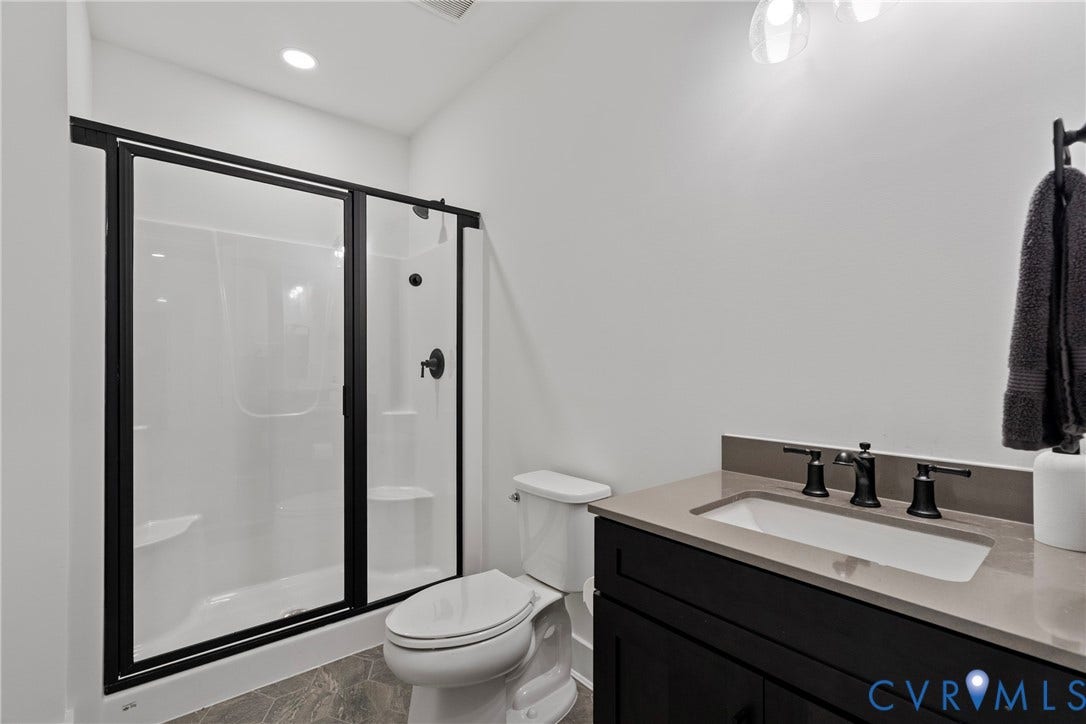18312 Barrin Court, Barrington, Moseley, VA 23120 Contemporary bathroom featuring a shower with black-framed glass sliding doors, a built-in white shower surround, and a coordinating black shower fixture