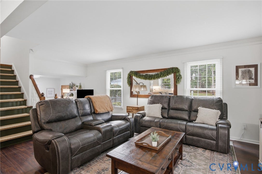 Spacious living area featuring dark wood-finish flooring, white walls, and crown molding