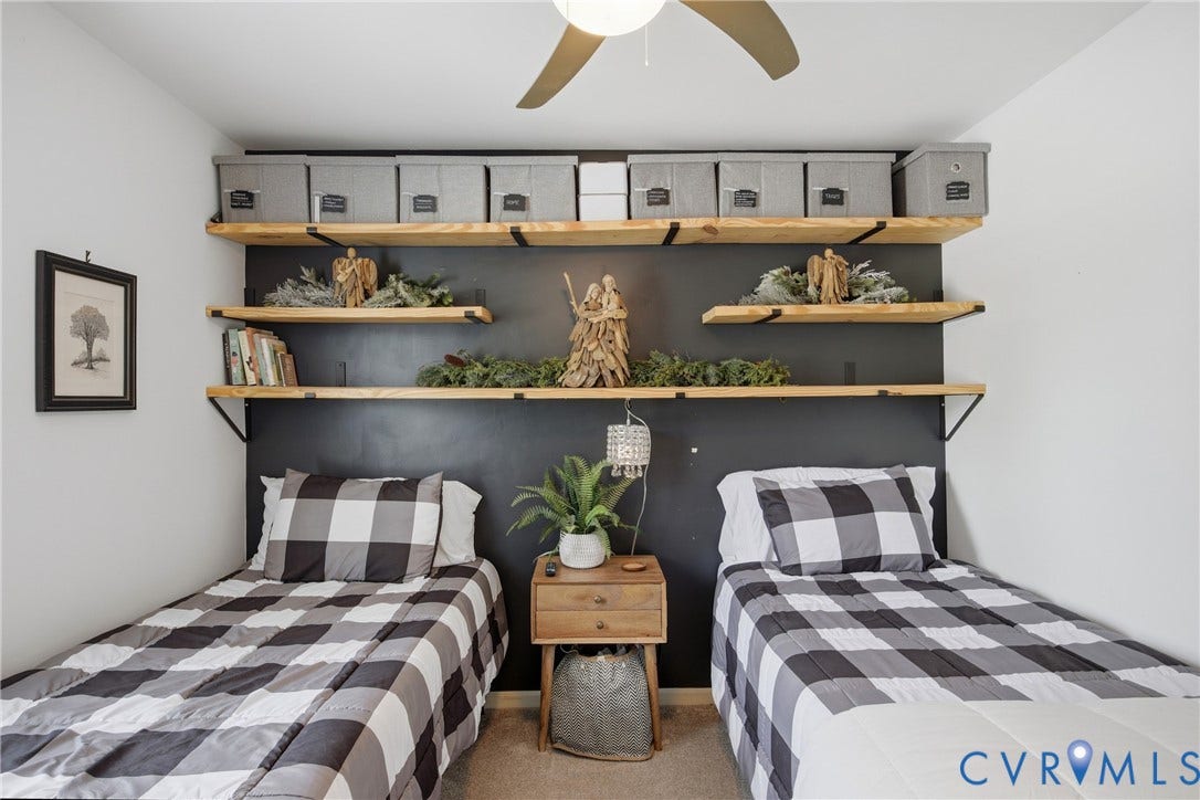 Bedroom featuring a ceiling fan, wood-finish floating shelves, and a dark accent wall