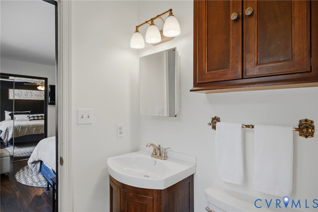 Bathroom vanity with a white countertop and brass-finish faucet, featuring a medicine cabinet and overhead three-bulb light fixture