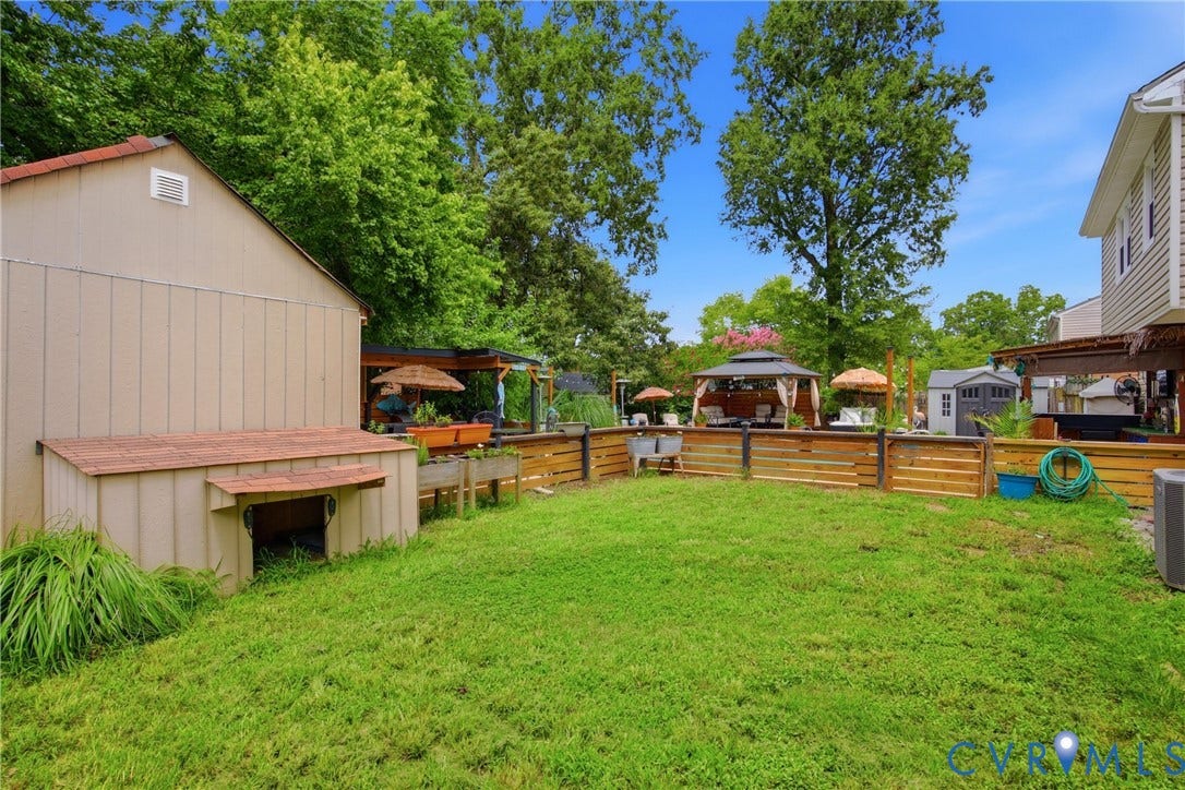 Expansive lawn area featuring a wood fence, a detached shed with a red-shingle roof, and a covered patio area with a gazebo
