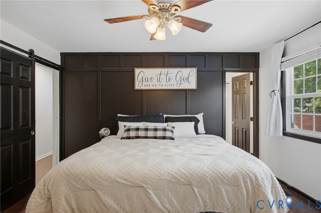 Bedroom featuring a decorative accent wall with panel molding, a ceiling fan with integrated lighting, a multi-pane window, and wood-finish flooring