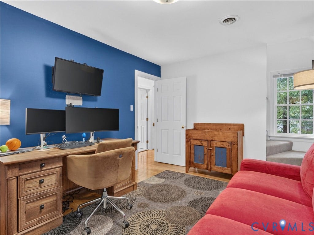 Hardwood flooring, painted accent wall, white trim, and a window with natural light