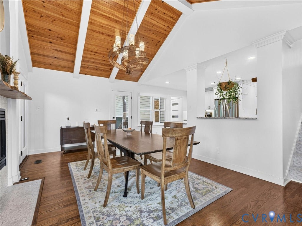 Vaulted wood-paneled ceiling with exposed beams, wood-finish flooring, fireplace with white surround, pass-through window with stone countertop, and French door