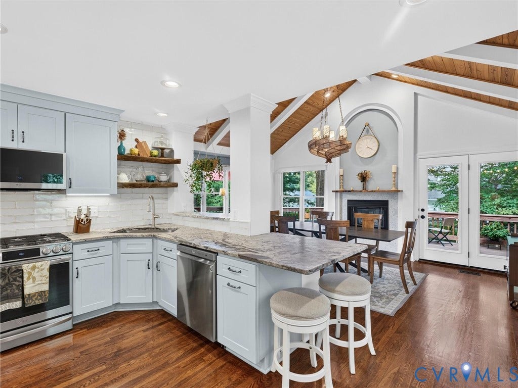 Light-toned cabinetry with stainless steel appliances, granite countertops, wood-finish flooring, and vaulted ceilings with exposed beams