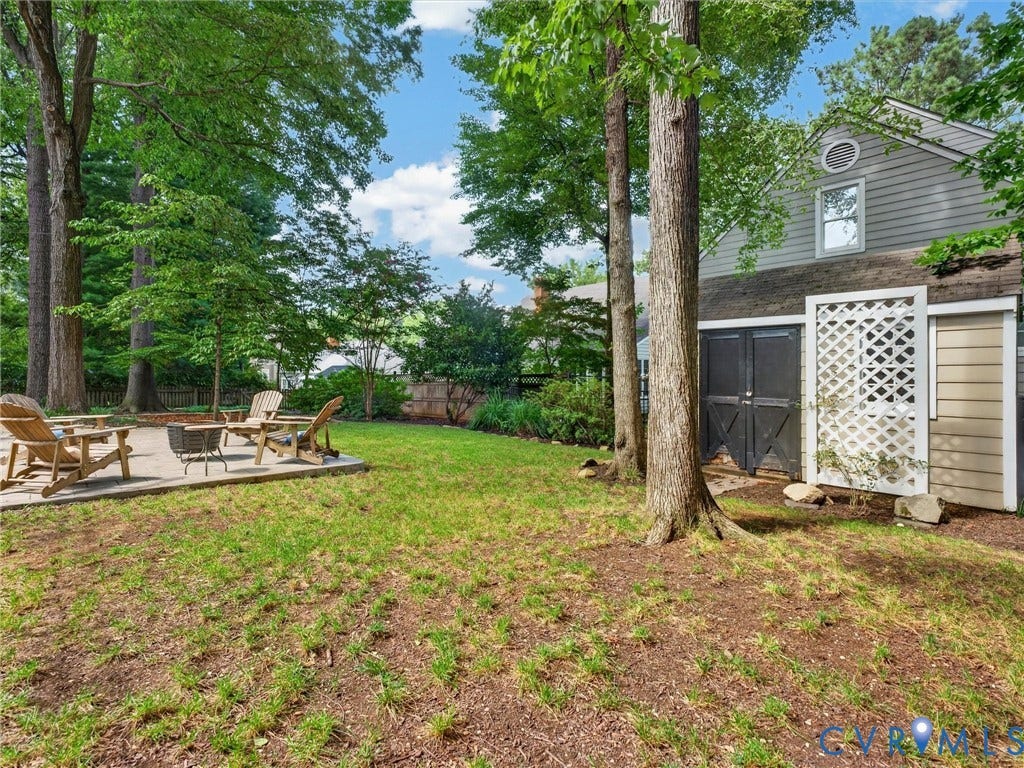 Expansive backyard featuring a concrete patio, mature trees, and a siding structure with a gable window