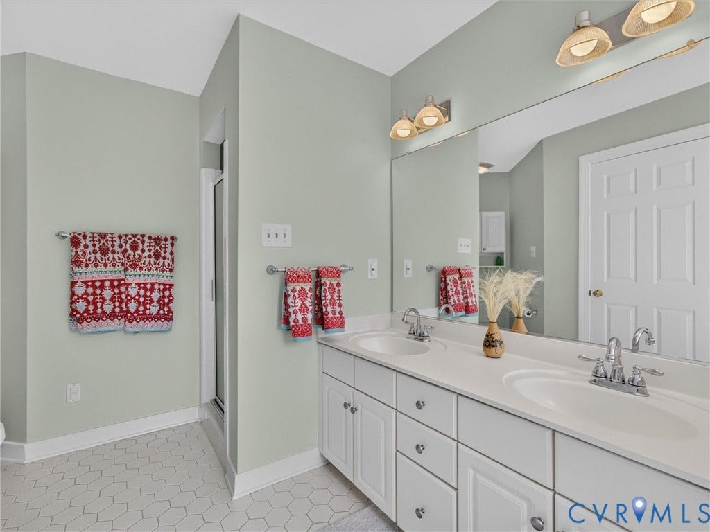 Dual vanity with integrated sinks, expansive wall-mounted mirror, white shaker-style cabinetry, chrome fixtures, and hexagonal floor tiling