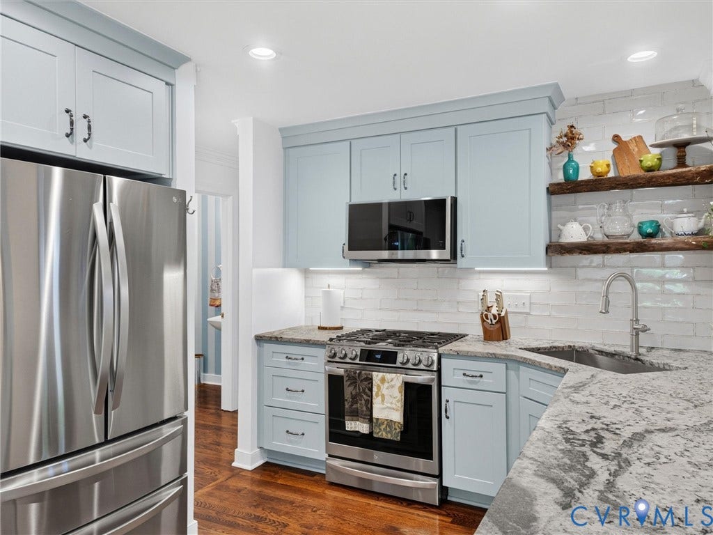 Stainless steel appliances, light blue cabinetry, white brick-patterned backsplash, wood-finish flooring, and light-toned countertops