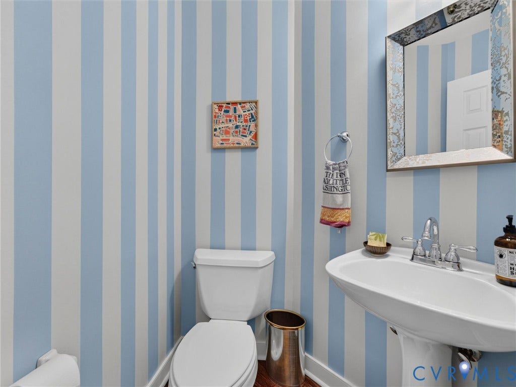 Pedestal sink with chrome faucet, wall-mounted mirror with decorative frame, and blue and white striped wall finish