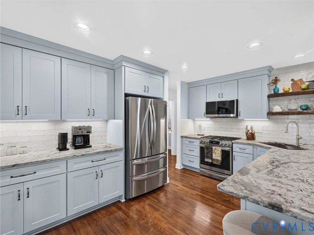 Wood-finish flooring, light blue cabinetry, stone countertops, stainless steel appliances, and a subway tile backsplash