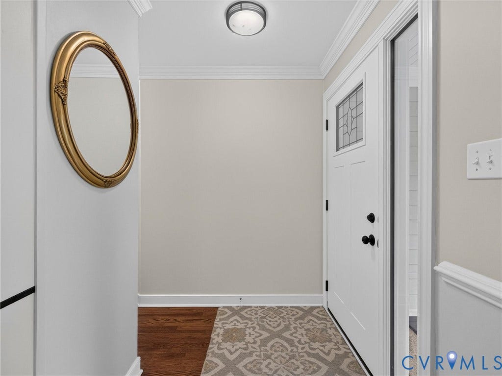 Welcoming foyer showcasing hardwood flooring, neutral wall finishes, recessed ceiling lighting, a decorative gold-framed circular mirror, and geometric patterned area rug accents